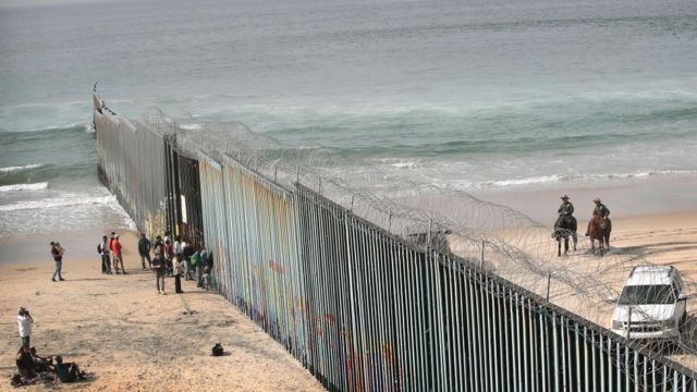 Migrantes junto a la valla fronteriza en Playas de Tijuana