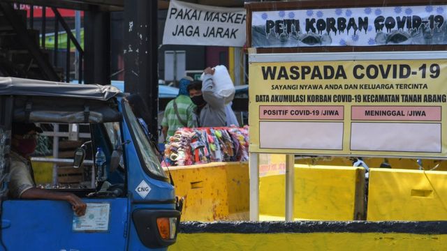 Warga melintasi replika peti mati dan papan himbauan waspada COVID-19 di kawasan Pasar Tanah Abang, Jakarta, Selasa (01/09).