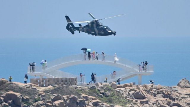 Tourists on China's Pingtan Island, the closest to Taiwan, watch a military helicopter during their country's maneuvers in response to Pelosi's trip.