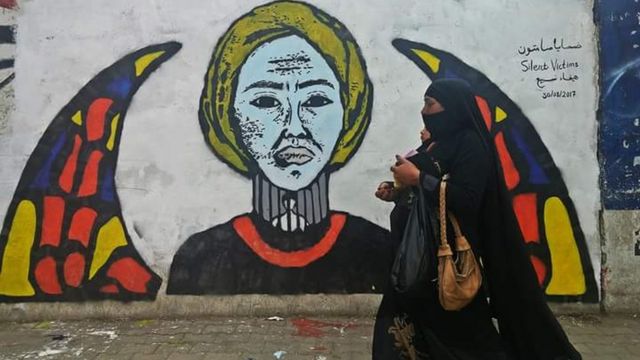 الجدارية تشرح معاناة أهالي المختفين قسريا وتصور امرأة في رقبتها قضبان خلفها شخص معتقل والقمرية-نافذة مستديرة زجاجها ملون- كناية عن اليمن حيث تعتبر علامة أساسية في العمارة اليمنية.