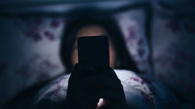 Chica leyendo en la cama un telefono