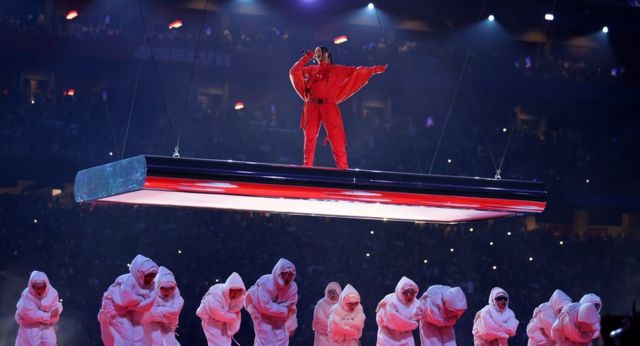 Rihanna en una plataforma flotante sobre un enjambre de enérgicos bailarines vestidos de blanco