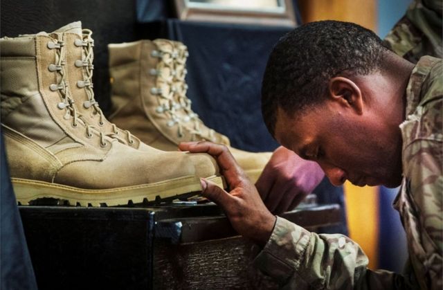 soldado americano cabisbaixo segura em duas botas de combate que estão à sua frente