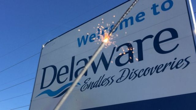 Una luz de bengala encendida frente a un letrero de bienvenida a Delaware.
