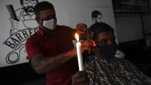A man holds a candle as he gets a hair cut in Colombo on August 17, 2020, during a lengthy electricity outage affecting the entire country of more than 21 million people. - Some 21 million people across Sri Lanka were without power on August 17 after an hours-long nationwide outage following a "unspecified failure" at a major power plant, the state-run electricity board said. (Photo by ISHARA S. KODIKARA / AFP) (Photo by ISHARA S. KODIKARA/AFP via Getty Images)