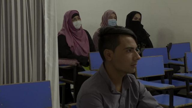 Three female students and one male student in a classroom separated by a curtain