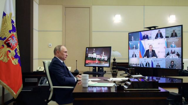 Vladimir Putin sentado em frente a duas telas