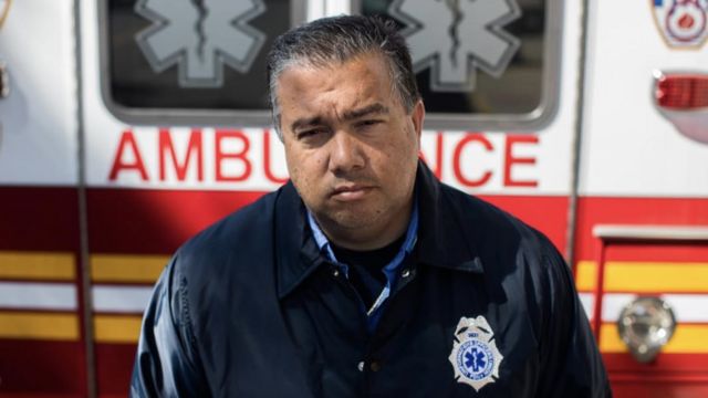 Anthony in front of the ambulance, staring sternly at the camera