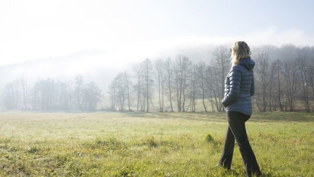 Mulher idosa caminha sozinha em um campo enevoado