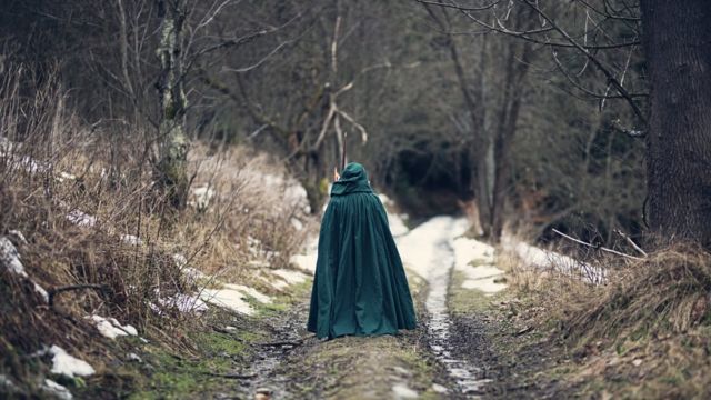 Persona con capa verde caminando sola en un bosque.