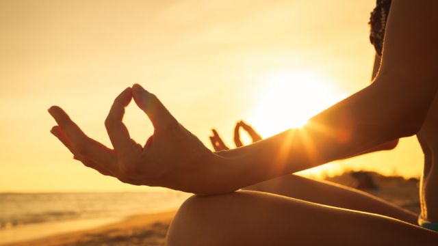 Manos de una mujer en posición de yoga durante una puesta de Sol