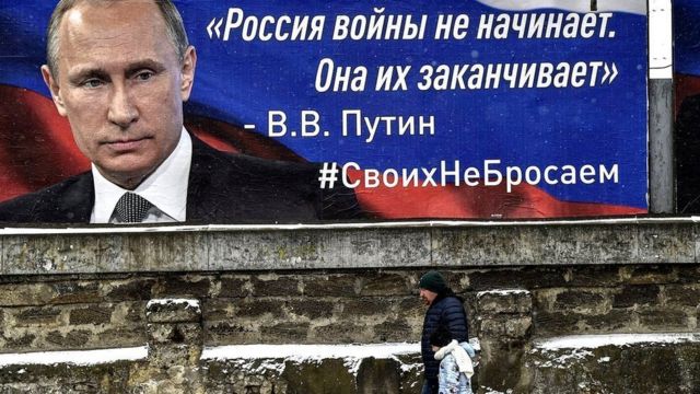 Pessoa caminha ao lado de outdoor com rosto de Putin