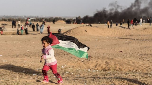 طفل فلسطينية ترفع العلم الفلسطيني قرب الحدود بين إسرائيل وقطاع غزة