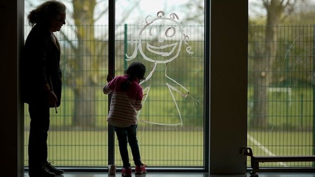 Foto de uma mulher e uma criança, que desenha uma pessoa sorrindo no vidro de uma janela