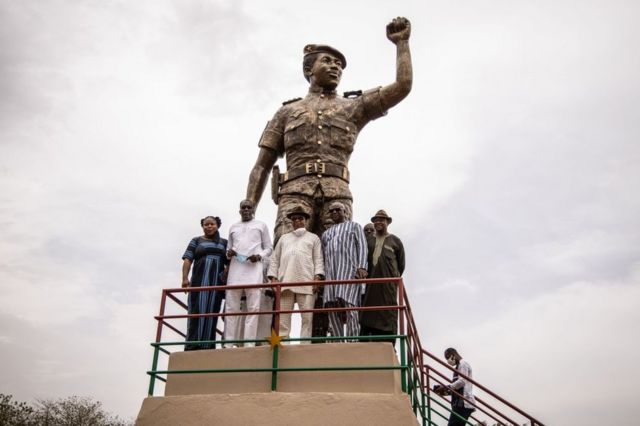 Officials pose for a photo beneath the second bronze statue of Burkina Faso's former President Thomas Sankara who was killed on October 15, 1987, at his memorial at the Conseil de l'Entente in Ouagadougou, on May 17, 2020. - This is the second time the statue is inaugurated after the first version has been removed because of complaints that it doesnt bear a resemblance to the national hero