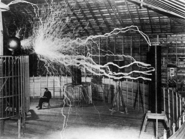 Inventor and scientist Nikola Tesla in his laboratory as his magnifying glass generates bolts of electricity.  December 1899.
