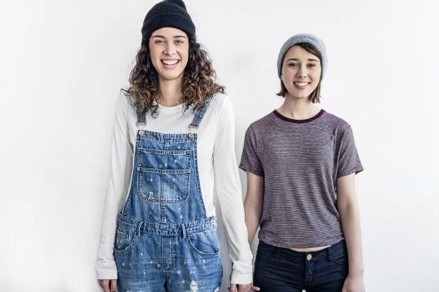 Smiling lesbian couple standing against white wall