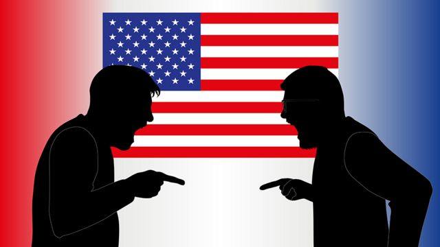 Dos personas discutiendo frente a una bandera de EE.UU.