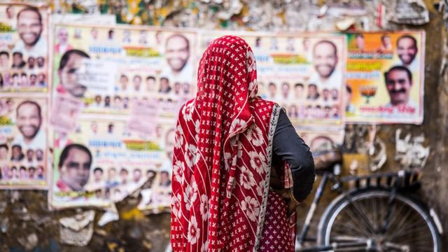 Mulher de costas olhando para cartazes de candidados na Índia