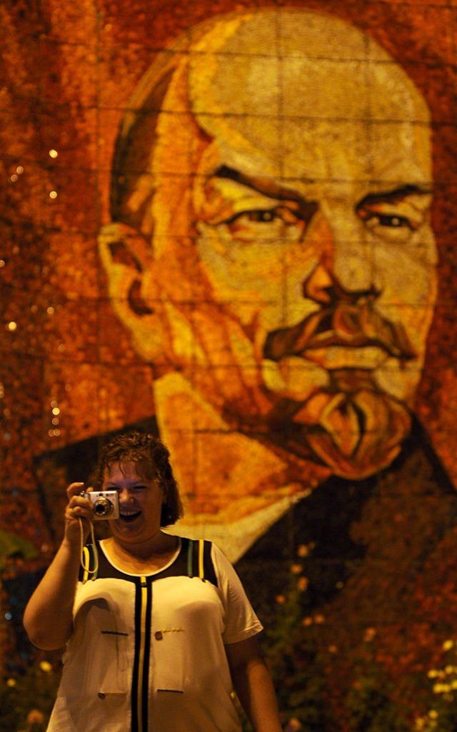 A Russian woman takes a photo while standing near a giant mosaic with the portrait of the founder of the Soviet Union, Vladimir Lenin, in Sochi.