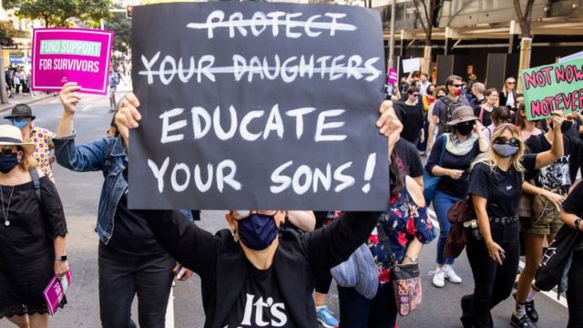 A protestor holds a sign saying 'educate your sons' with the words 'protect your daughters' crossed out