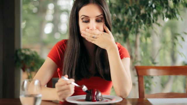 Mujer comiéndose un pastel de chocolate sintiéndose mal