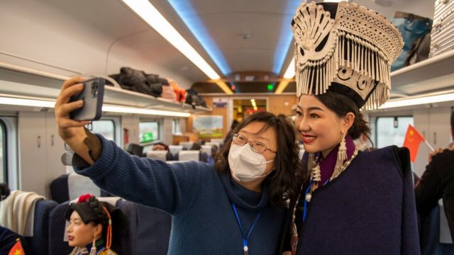 12月26日，连接成都和昆明的新成昆铁路开通，带着口罩的乘客与穿着彝族传统服饰的女性自拍合照。消费低迷是目前中国经济面临的难题之一。(photo:BBC)