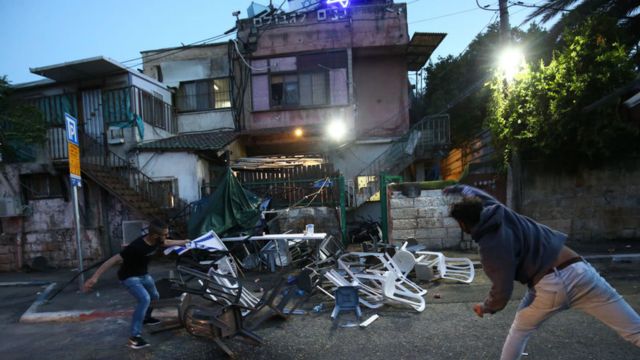 Two men throw chairs at a house with the Israeli flag in Sheikh Zarra
