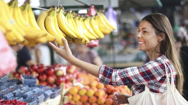 Mujer comprando bananas en un mercado.
