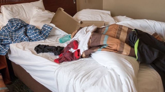 Una cama desarreglada con ropa y una caja de cartón encima.