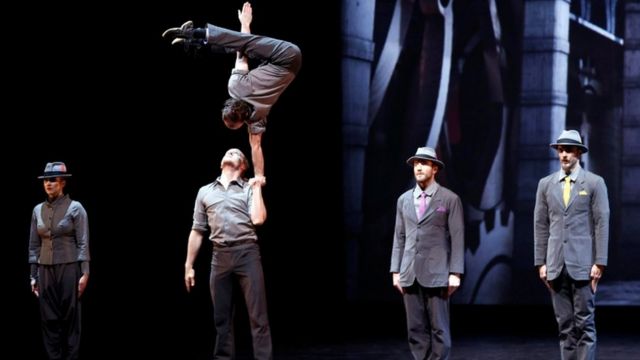 A group of circus performers: one man balances on another's palm,
