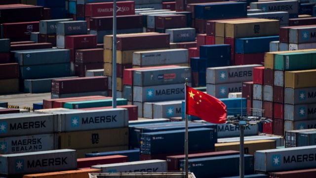Una bandera china ondea rodeada de decenas de contenedores.