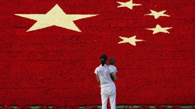 A woman holds her son as she looks at the national flag made up of 100,000 carnations at Wuling Square September 25, 2007 in Hangzhou, China