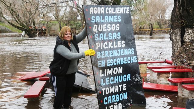 Mujer en Argentina sostiene un cartel con una lista de verduras en una una calle inundada