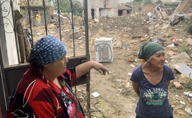 Svetlana Kharlanova (left), 67, stands in front of her cottage near a deep crater left by a missile in her yard in Mykolaiv