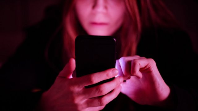 A woman is bathed in pink light as she looks at her phone in her hand