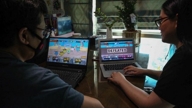 شخصان يلعبان لعبة آكسي انفينيتي على جهاز كمبيوتر.