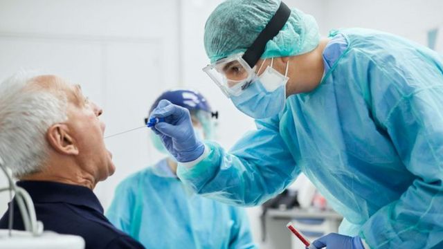 Especialista insere bastonete na boca de paciente para fazer um teste de covid-19
