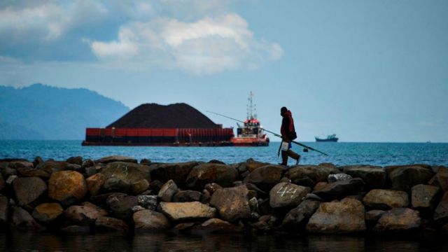 인도네시아 해안 도시 반다 아체의 한 어부가 방파제 위를 걷고 있다. 뒤로는 석탄을 실은 바지선이 보인다