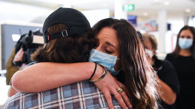 امرأة ترتدي كمامة للوجه وهي تعانق حبيبها في مطار كينغسفورد سميث في سيدني بعد قدومها من نيوزيلندا في أكتوبر/تشرين الأول 2020 ، أستراليا.
