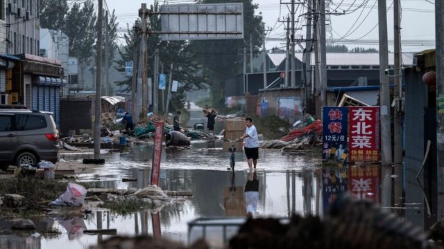 A man carries boxes of goods salvaged from a local business on a bicycle as he wades through receding floodwaters on August 5, 2023 in Zhuozhou, Hebei Province south of Beijing, China.