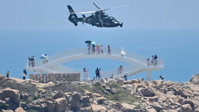 Turistas miran helicópteros chinos sobrevolando la isla de Pingtan.