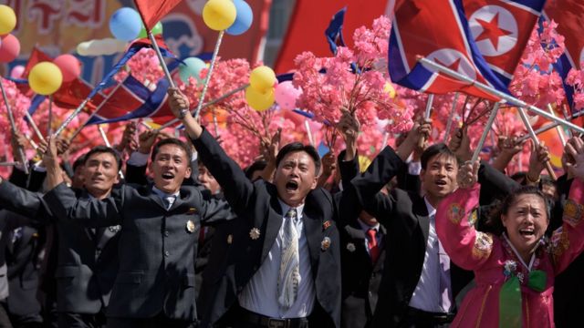 parade participants wave flowers as they pass Mr Kim