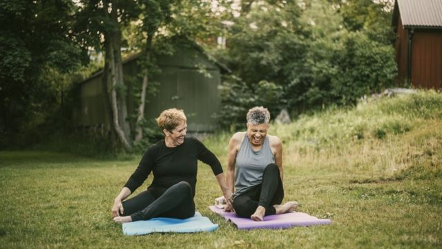 Dos mujeres en el campo sentadas en esterillas de hacer yoga