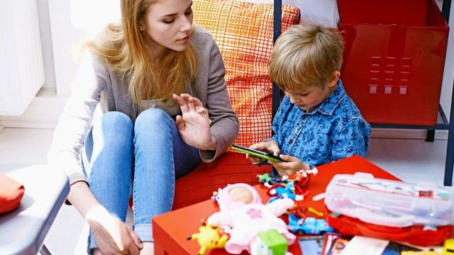 Niñera con un niño y un dispositivo electrónico.