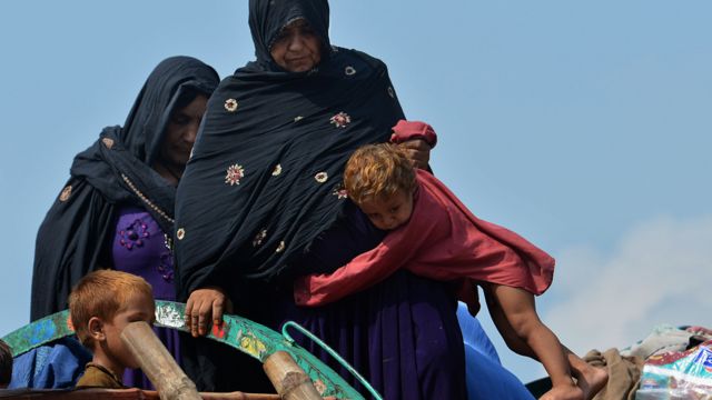 Dos mujeres intentan subir con un niño a un camión con sus pertenencias
