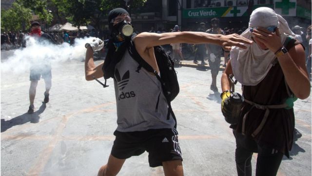 Manifestante lanza de vuelta el gas lacrimógeno tirado por la policía cerca del centro comercial Costanera Center