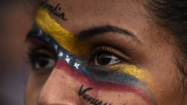 Imagen muy cerrada de los ojos de una mujer con la bandera colombiana y venezolana pintada en el rostro y las palabras 