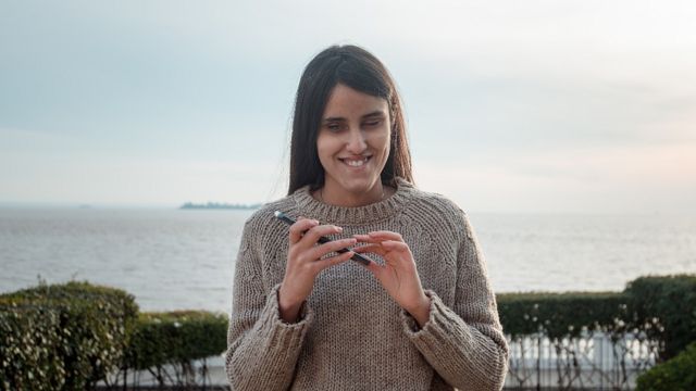 Milagros Costabel con su celular, por detrás se ve el Río Uruguay