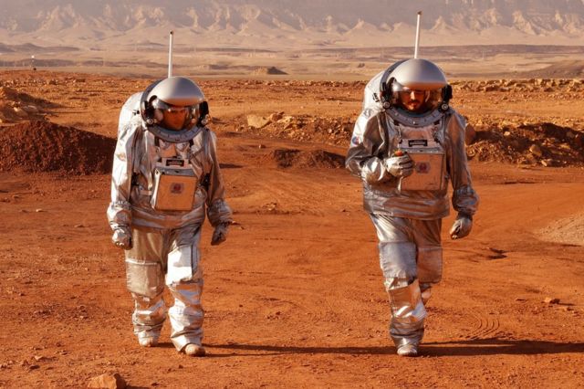 Two astronauts walk in spacesuits during a training mission for planet Mars at a site that simulates an off-site station at the Ramon Crater in Mitzpe Ramon in Israel's Negev desert